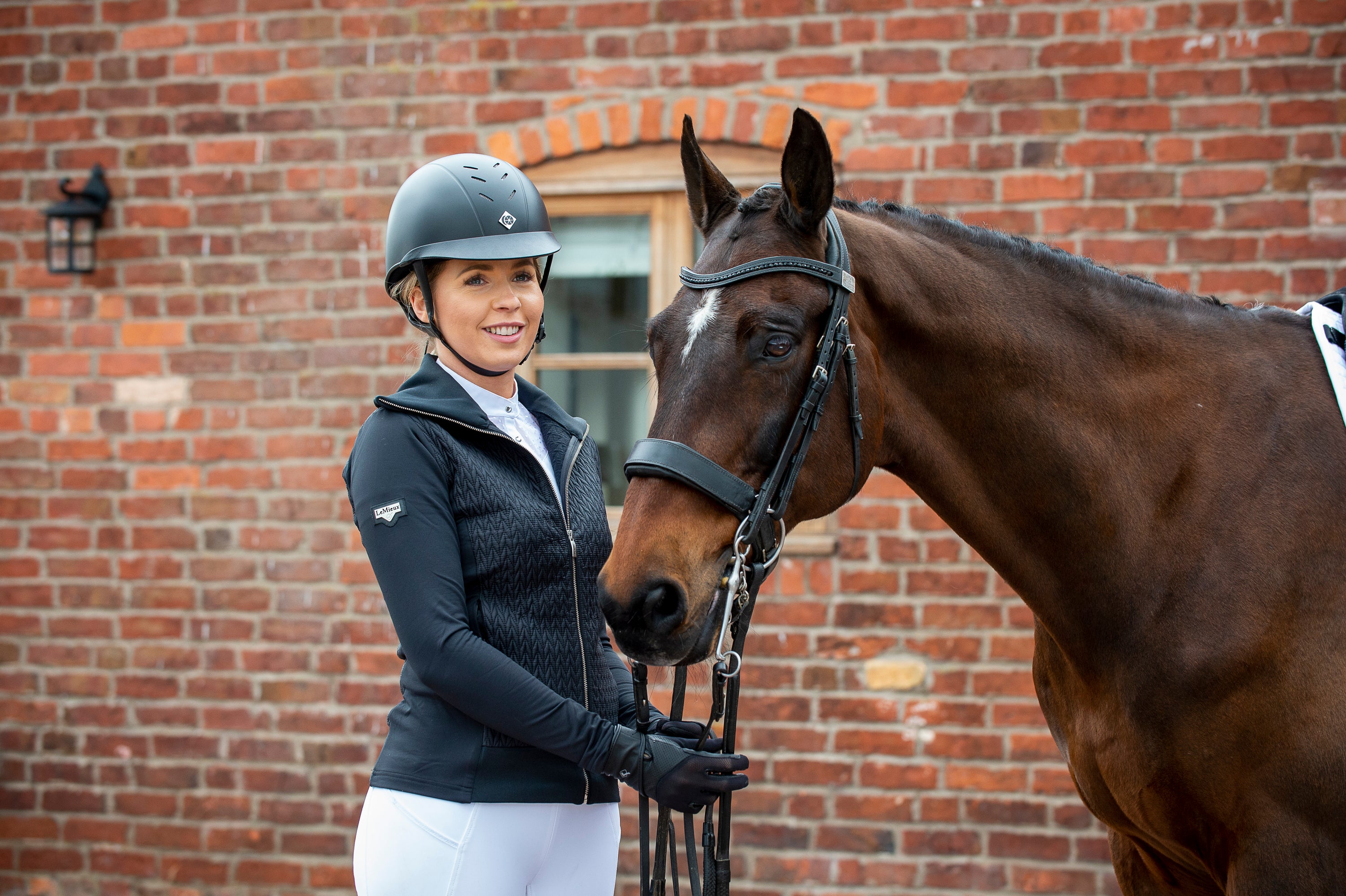 equine helmet accessories, woman in black charles owen helmet stands with bay horse
