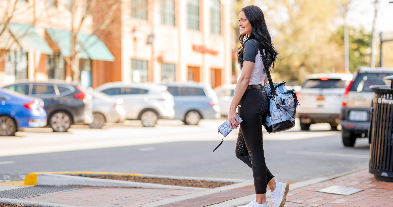 Girl with black hair wearing horse riding apparel, equestrian clothing, equestrian fashion waits to cross the street in cute downtown area