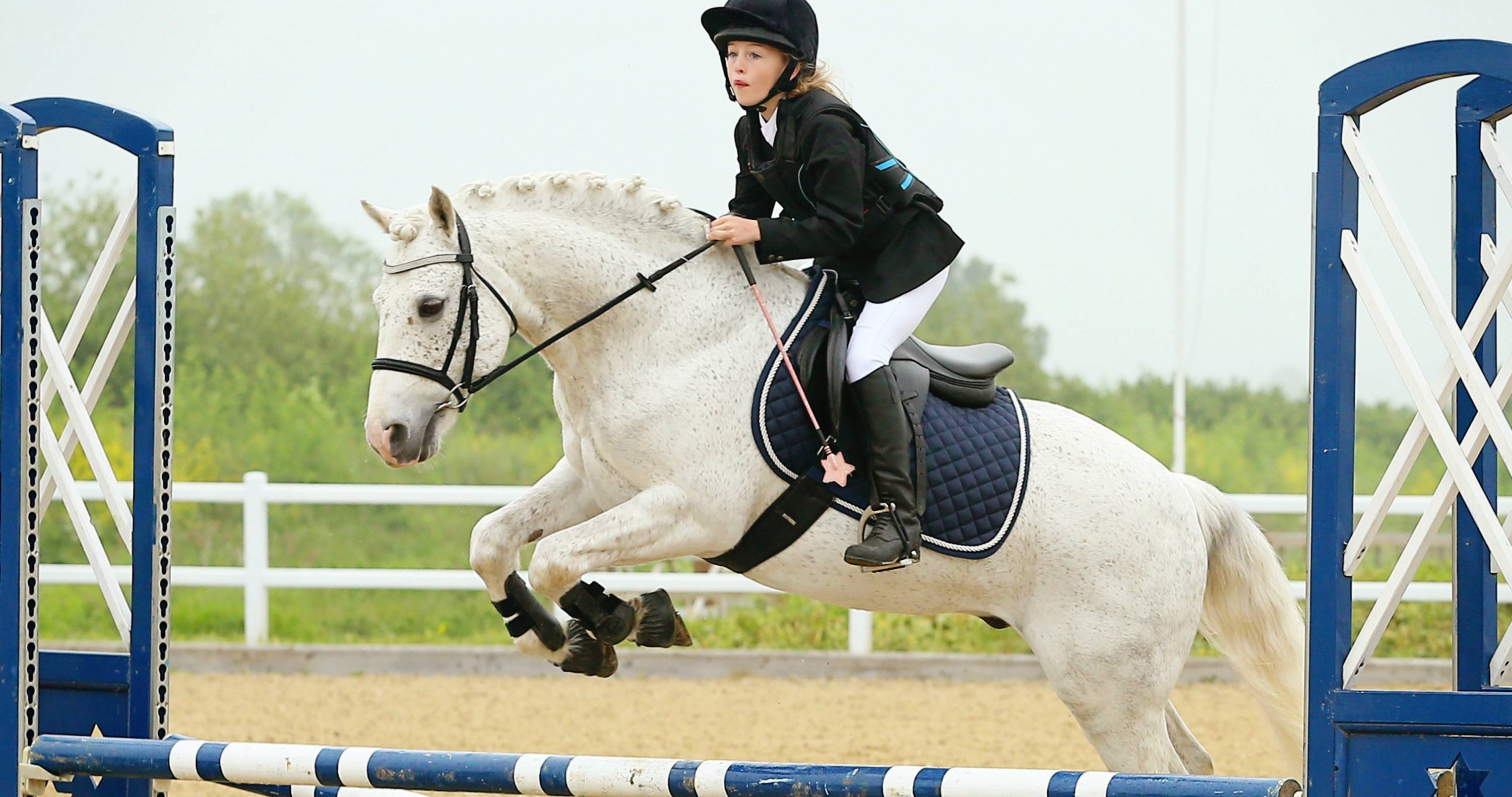 young girl ride white pony over a blue and white fence at a horse show, Children's riding stirrups, horse riding equipment, stirrups