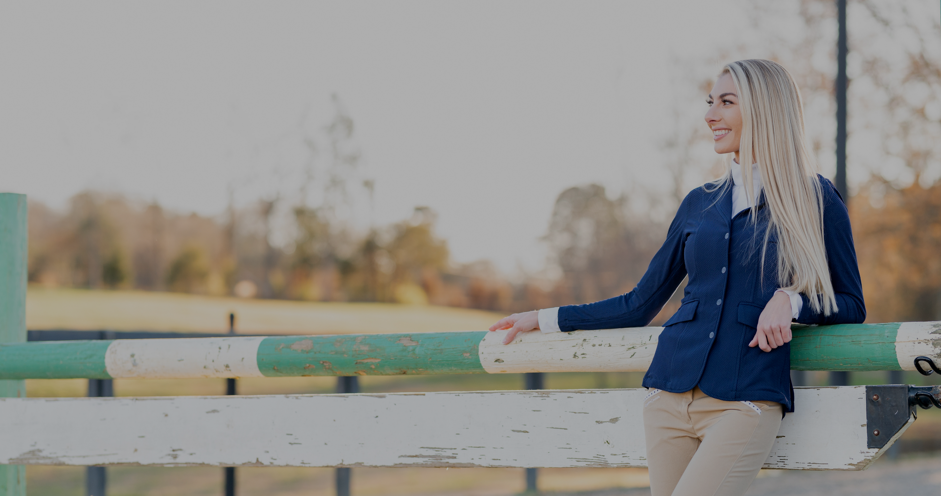 blonde equestrian leaning back against green and white fence wearing a hunter horse show outfit