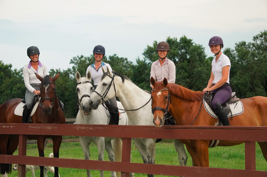four equestrians wearing various colors of horse riding helmets